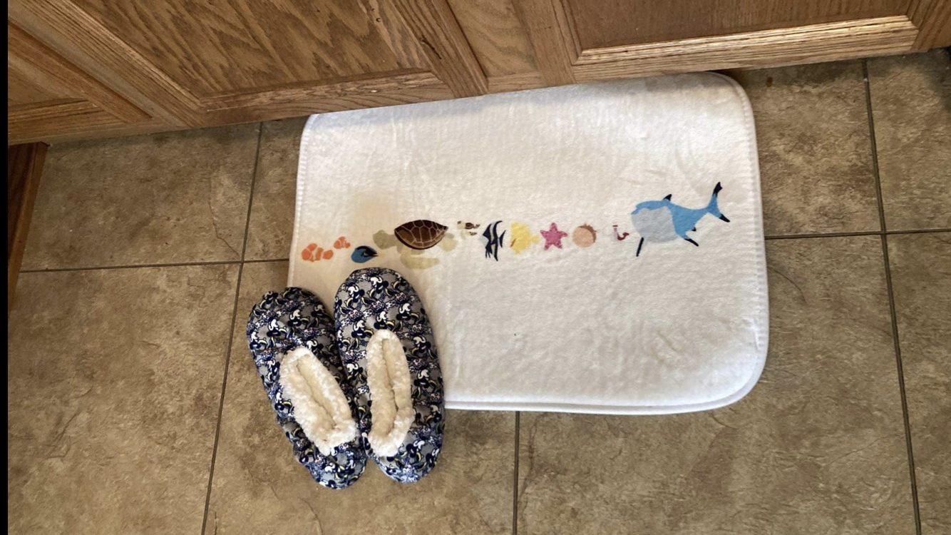 White bathmat featuring water color art of the movie's characters and a pair of slippers resting on it.